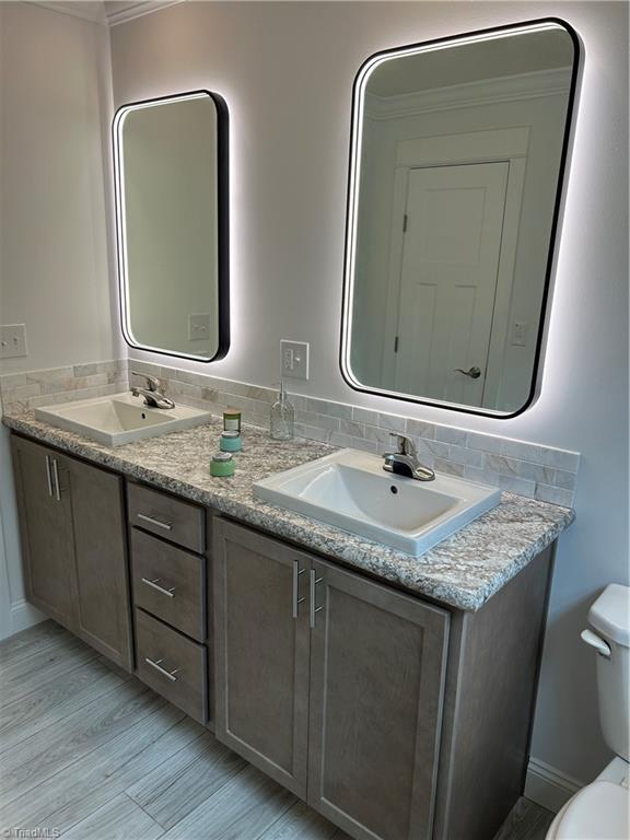 bathroom featuring vanity, toilet, ornamental molding, and backsplash