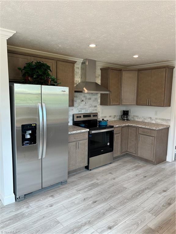 kitchen with light wood-type flooring, appliances with stainless steel finishes, a textured ceiling, and wall chimney exhaust hood