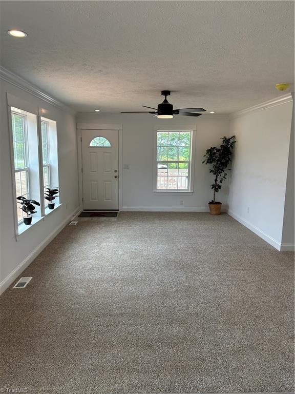 carpeted entryway featuring ceiling fan, crown molding, and a textured ceiling