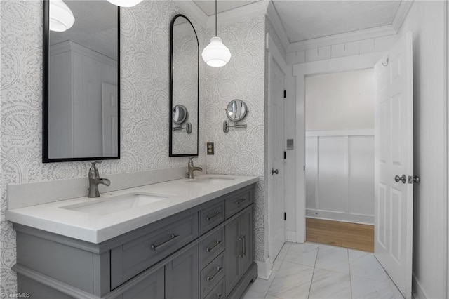 full bath with double vanity, wallpapered walls, crown molding, and a sink