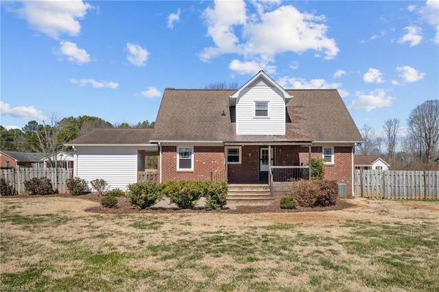 rear view of property featuring fence, a porch, a lawn, and brick siding