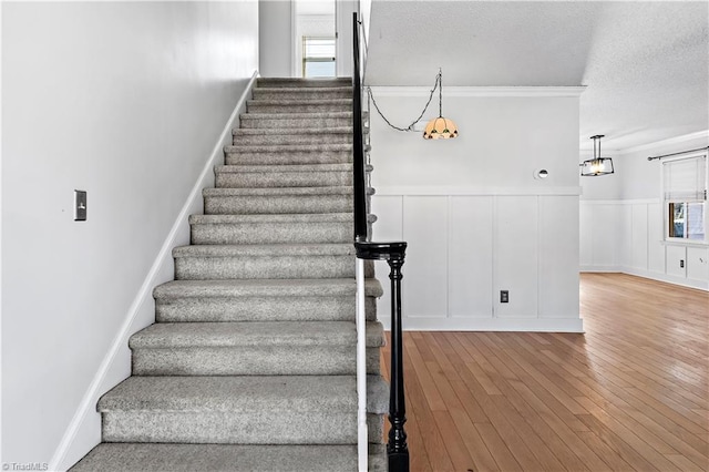 stairway featuring a decorative wall, ornamental molding, wainscoting, a textured ceiling, and wood finished floors