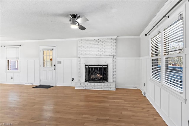 unfurnished living room with a textured ceiling, ornamental molding, light wood-type flooring, a fireplace, and ceiling fan