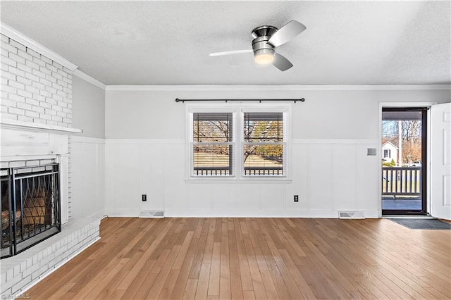 unfurnished living room featuring visible vents, wood-type flooring, a textured ceiling, crown molding, and a brick fireplace