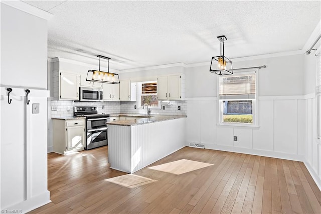 kitchen with appliances with stainless steel finishes, white cabinetry, decorative light fixtures, and kitchen peninsula