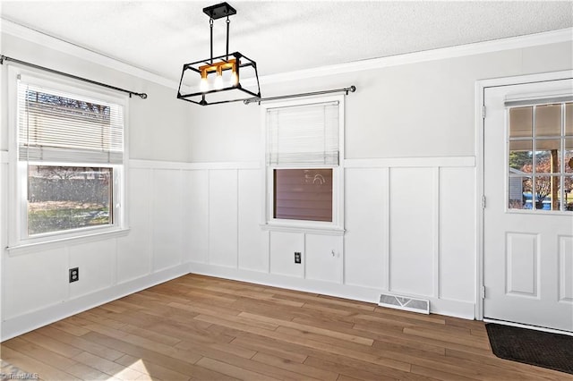 unfurnished dining area featuring hardwood / wood-style flooring, a textured ceiling, ornamental molding, and a wealth of natural light