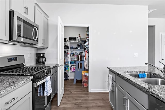 kitchen with dark wood-style flooring, appliances with stainless steel finishes, a sink, decorative backsplash, and gray cabinetry