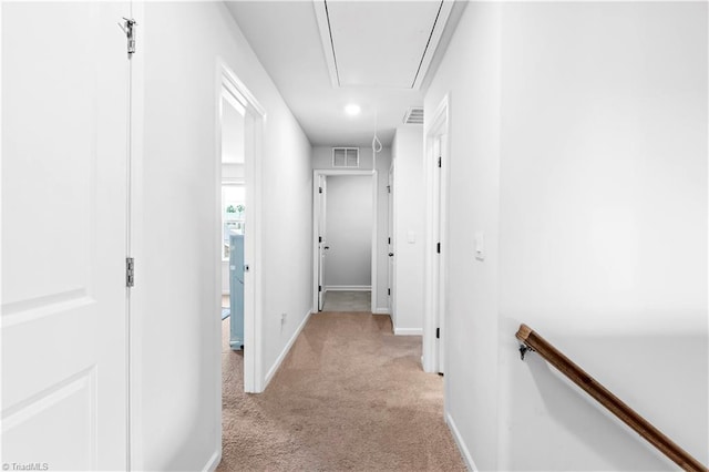 hallway featuring visible vents, attic access, baseboards, and light carpet