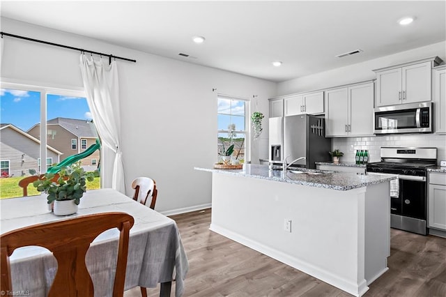 kitchen with appliances with stainless steel finishes, light stone counters, a sink, an island with sink, and visible vents
