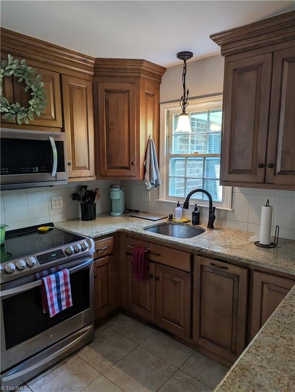 kitchen with decorative backsplash, light stone counters, light tile patterned floors, stainless steel appliances, and sink