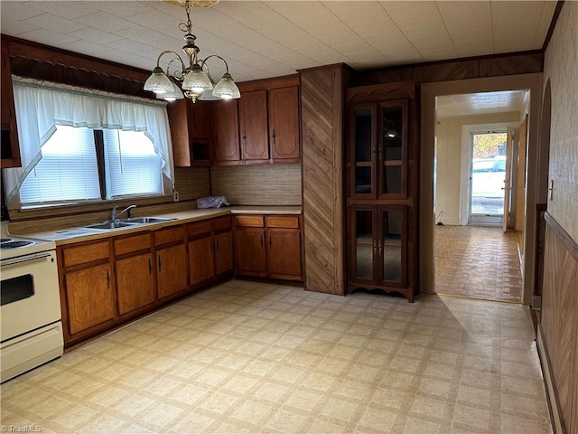 kitchen with wooden walls, sink, decorative light fixtures, a notable chandelier, and white electric range