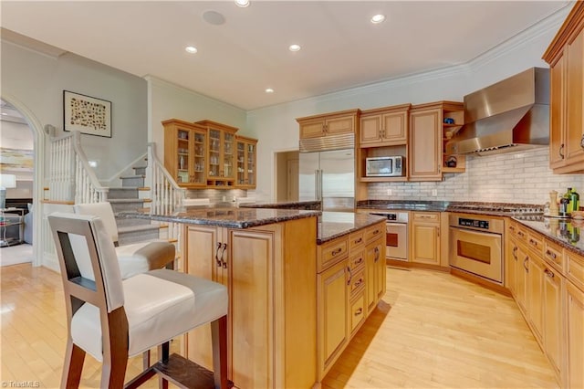 10 Sunfish Pt, Greensboro, NC 27455 - kitchen featuring stainless steel appliances, wall chimney exhaust hood, a center island, light wood-type flooring, and crown molding