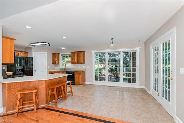 4335 Clovelly Dr, Greensboro, NC 27406 - kitchen featuring black appliances, light countertops, a breakfast bar, brown cabinets, and a peninsula