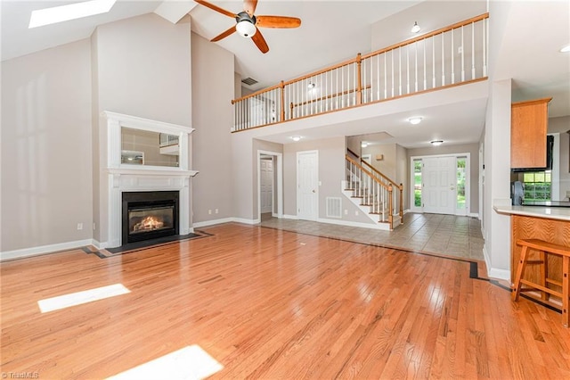 4335 Clovelly Dr, Greensboro, NC 27406 - unfurnished living room featuring stairs, light wood-style flooring, high vaulted ceiling, a fireplace with flush hearth, and ceiling fan