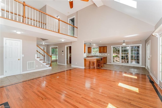4335 Clovelly Dr, Greensboro, NC 27406 - unfurnished living room with light wood-style flooring, high vaulted ceiling, stairway, ceiling fan, and a skylight