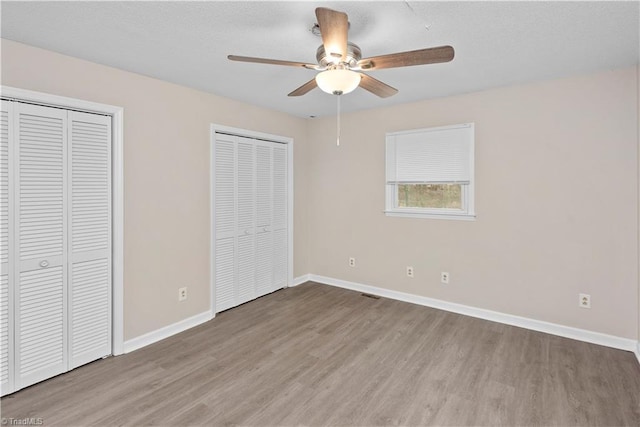 unfurnished bedroom with two closets, hardwood / wood-style flooring, and ceiling fan