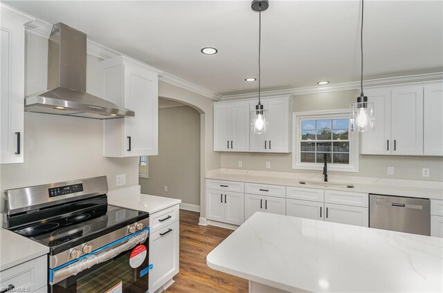 kitchen featuring stainless steel appliances, wall chimney range hood, light hardwood / wood-style floors, decorative light fixtures, and white cabinets