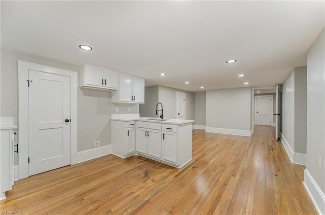 kitchen featuring white cabinetry, light wood-type flooring, kitchen peninsula, and sink