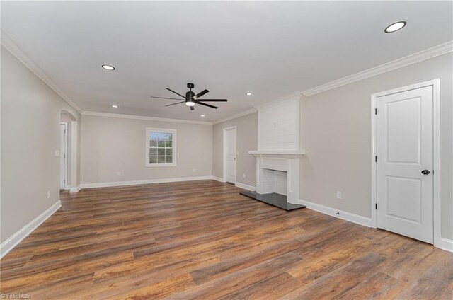 unfurnished living room with a large fireplace, dark hardwood / wood-style floors, ceiling fan, and crown molding