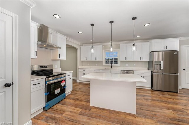 kitchen with pendant lighting, white cabinetry, wall chimney range hood, and appliances with stainless steel finishes