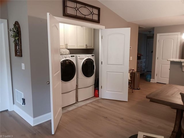 laundry area with washing machine and dryer, cabinets, and light hardwood / wood-style floors