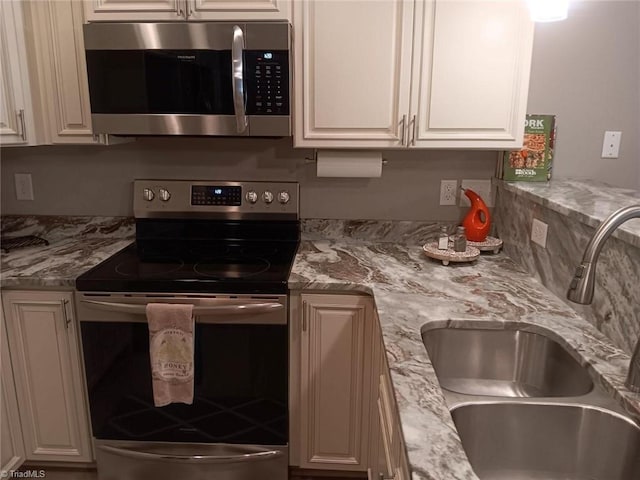 kitchen with decorative backsplash, light stone counters, stainless steel appliances, sink, and white cabinetry