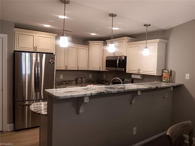 kitchen featuring kitchen peninsula, decorative light fixtures, stainless steel appliances, and dark stone counters