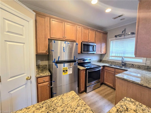 kitchen featuring ornamental molding, light wood-type flooring, appliances with stainless steel finishes, light stone countertops, and sink