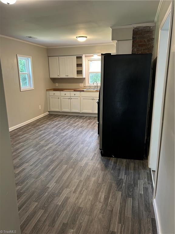 kitchen with ornamental molding, white cabinetry, sink, dark hardwood / wood-style floors, and black fridge