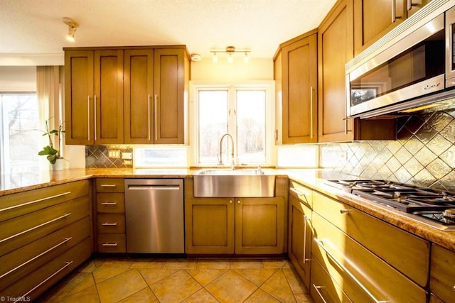 kitchen with light stone counters, stainless steel appliances, a healthy amount of sunlight, sink, and light tile patterned flooring