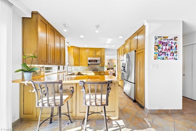 kitchen with kitchen peninsula, appliances with stainless steel finishes, backsplash, and a breakfast bar area