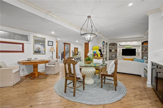 dining space featuring light hardwood / wood-style floors, ornamental molding, an inviting chandelier, and built in shelves