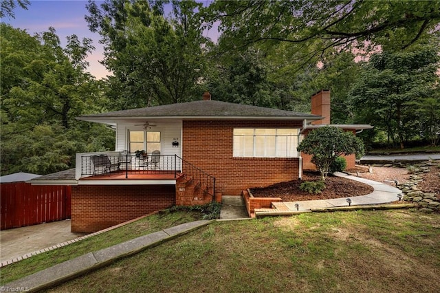 back house at dusk with a lawn, ceiling fan, and covered porch