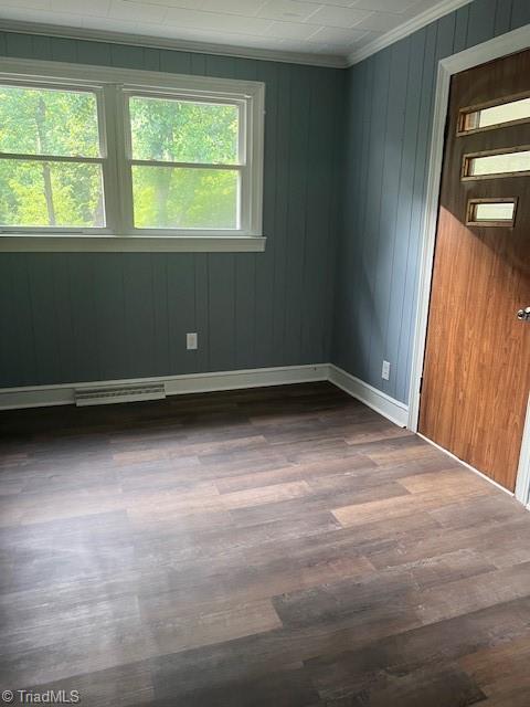 empty room featuring ornamental molding, dark hardwood / wood-style flooring, a wealth of natural light, and wooden walls