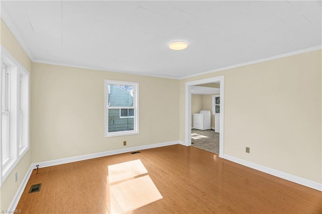 spare room featuring visible vents, baseboards, ornamental molding, wood finished floors, and washer and dryer