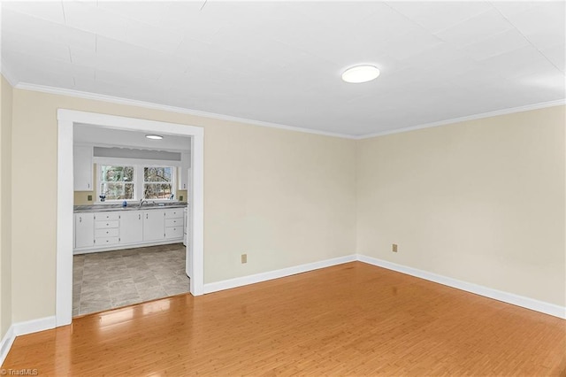 unfurnished room featuring crown molding, baseboards, light wood finished floors, and a sink