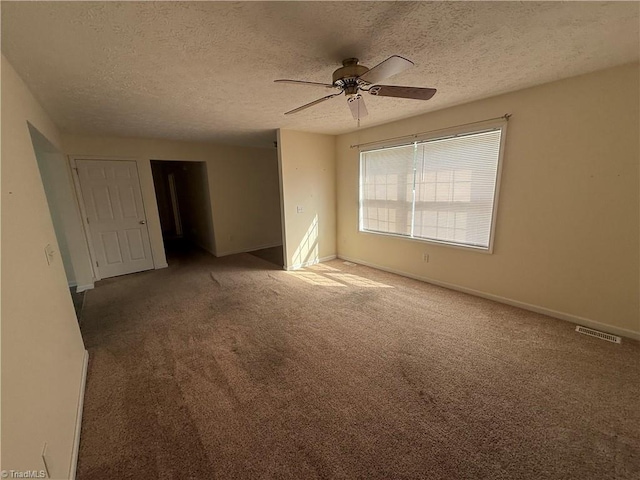 carpeted empty room with a textured ceiling, ceiling fan, visible vents, and baseboards