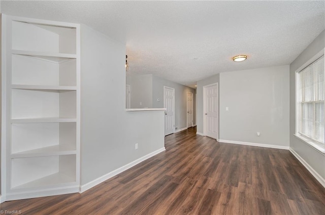 unfurnished room with built in shelves, dark wood-type flooring, a textured ceiling, and baseboards