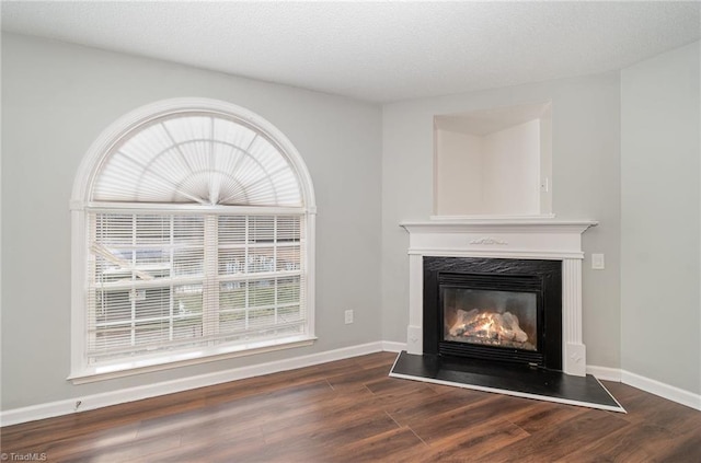 unfurnished living room with dark wood-type flooring, a glass covered fireplace, and a healthy amount of sunlight