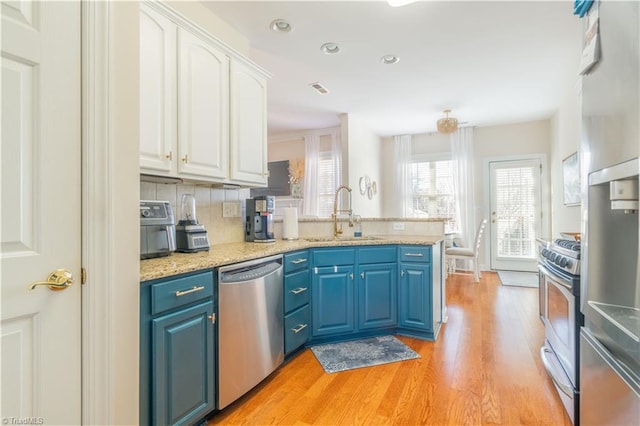 kitchen with appliances with stainless steel finishes, tasteful backsplash, sink, blue cabinetry, and white cabinetry