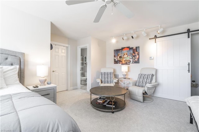 bedroom featuring a barn door, light colored carpet, ensuite bath, and ceiling fan