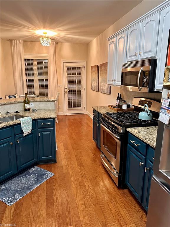 kitchen with blue cabinetry, sink, light stone countertops, and stainless steel appliances