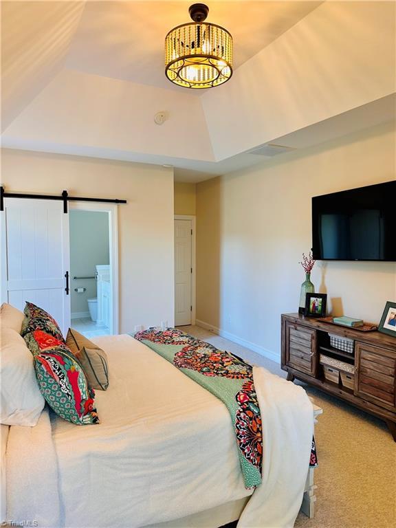 bedroom featuring carpet, a barn door, ensuite bathroom, and a raised ceiling