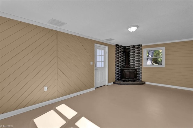 unfurnished living room with concrete floors, a wood stove, and wooden walls