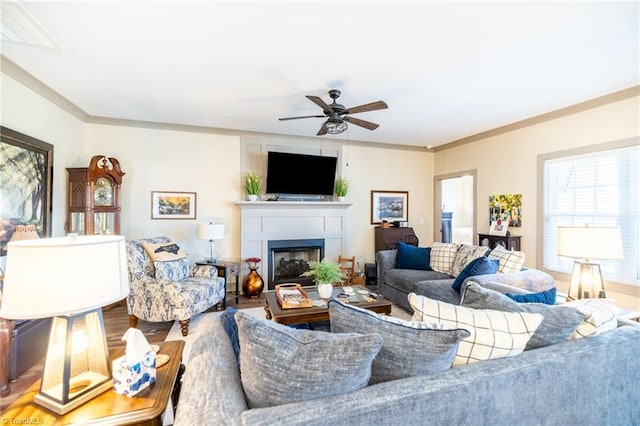 living area with ornamental molding, a fireplace, a ceiling fan, and wood finished floors