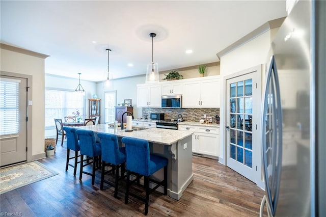 kitchen featuring a breakfast bar area, an island with sink, a sink, stainless steel appliances, and white cabinetry