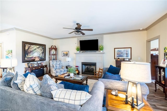 living area featuring a fireplace, crown molding, wood finished floors, and a ceiling fan