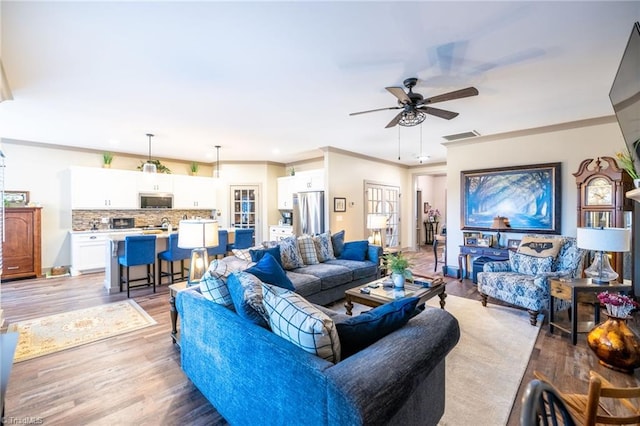 living room with baseboards, visible vents, light wood-style flooring, ceiling fan, and crown molding