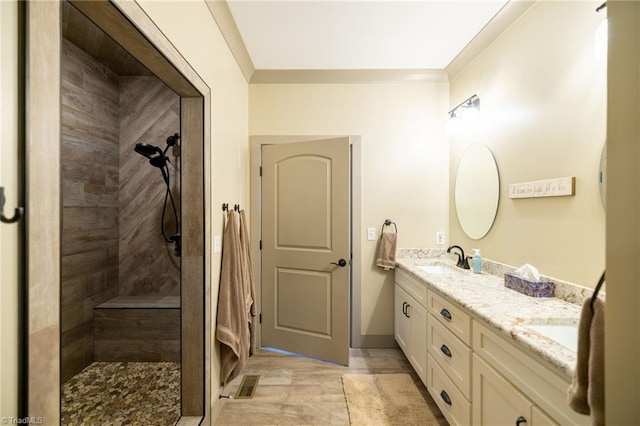 bathroom with a sink, visible vents, double vanity, and a tile shower