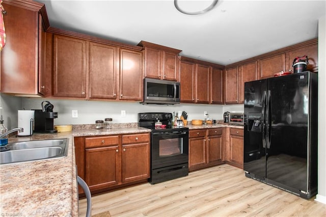 kitchen with brown cabinets, a sink, light wood-type flooring, black appliances, and light countertops